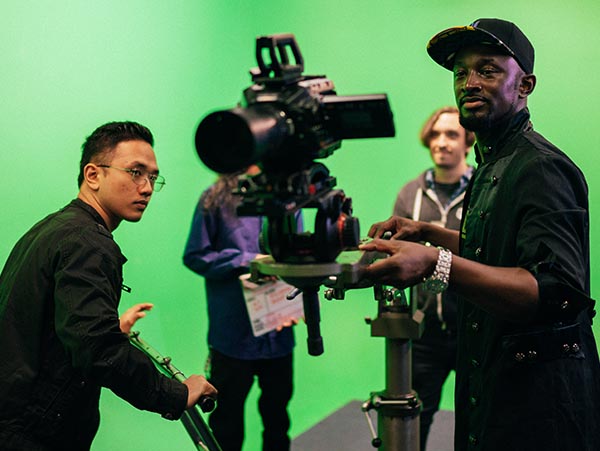 A group picture of a film crew operating a camera, directing, and filming in a studio with green screen.