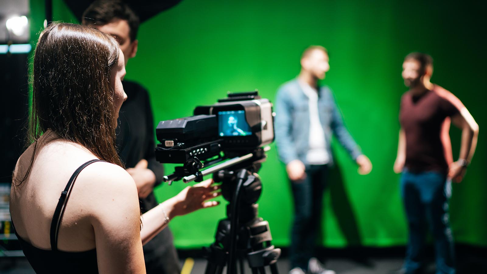A close-up of a student operating a camera in a film studio with green screen.