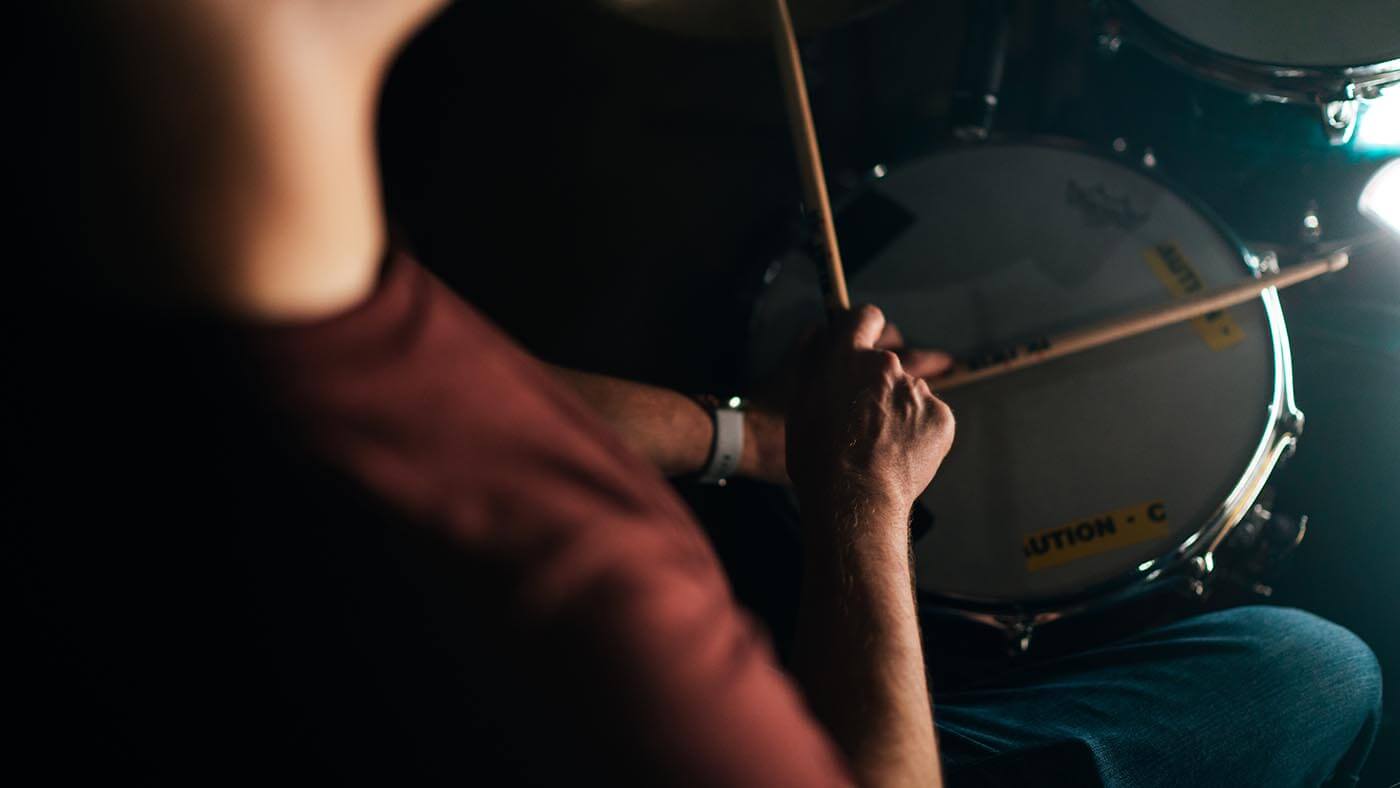 A close-up picture of a student holding drumsticks and playing drums.